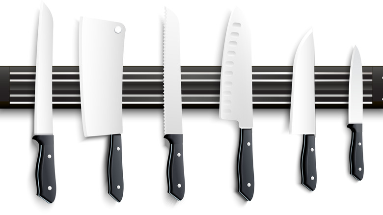 Variety of knives with a black handle on a magnetic strip against a white background