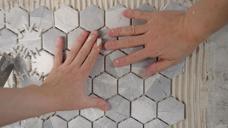 A pair of hands sticking adhesive tiles on the wall