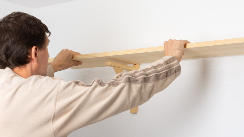 A man hanging a wooden shelf on a white wall