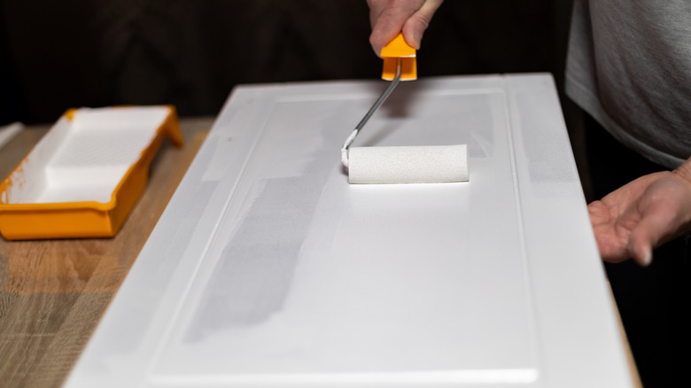 A person using a paint roller to apply white paint on a cabinet door