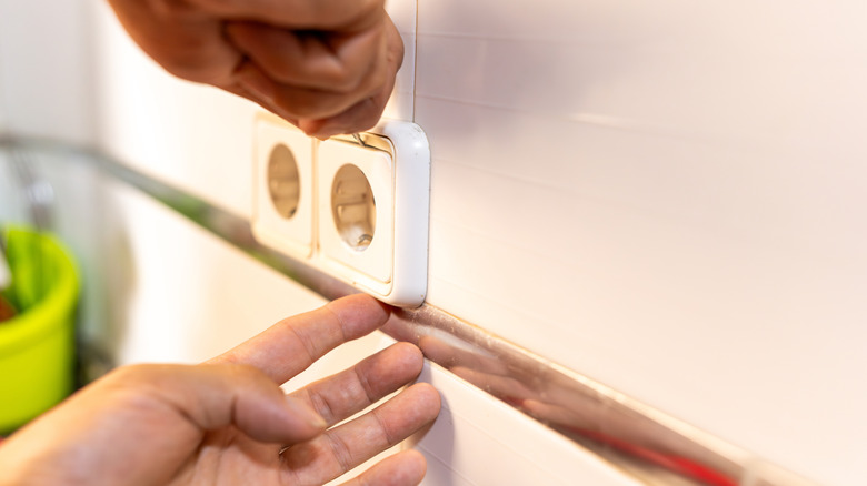 A pair of hands removing an outlet cover with a screwdriver