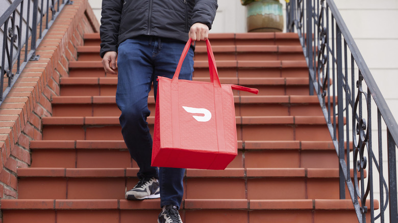 Delivery driver holding DoorDash bag while walking down stairs