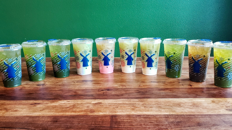 Ten matcha beverages from Dutch Bros on a wooden table.