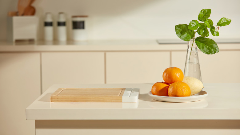 Kitchen countertop styled with wooden cutting board, fruit plate, and glass vase