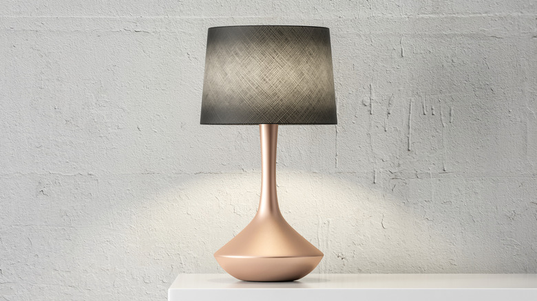 Stylish lamp placed on a white table against a textured wall