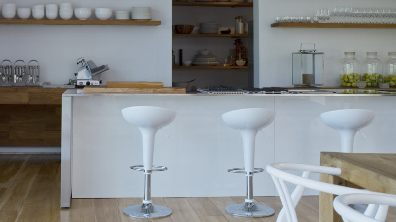 Several white bar stools arranged next to a kitchen island