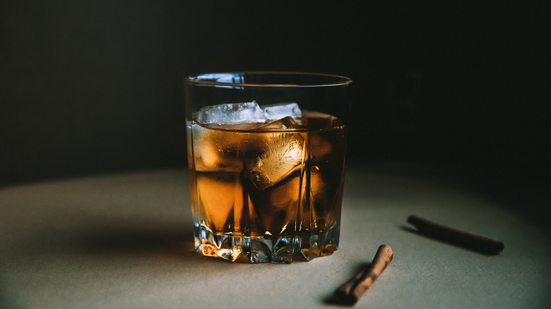 Cognac in a glass tumbler with a plain background and cinnamon sticks on the side