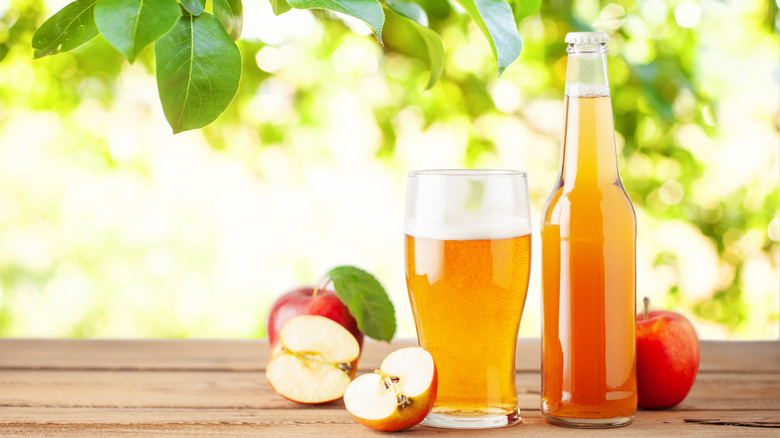 A glass and a bottle of cider shown next to each other surrounded by apples