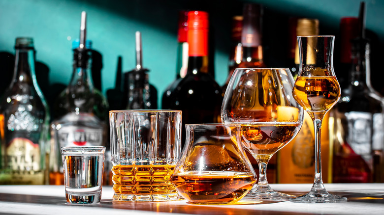A collection of different types of alcohol shown in glasses with bottles shown in the background