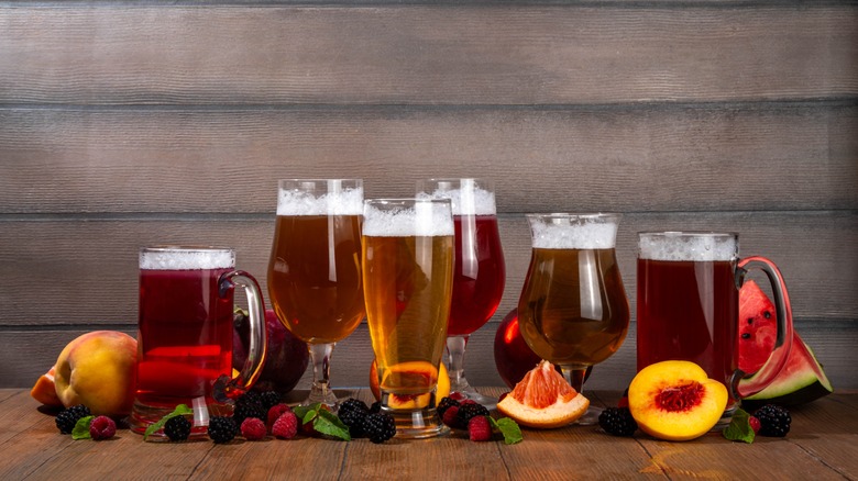 Various types of beer shown in large glasses and surrounded by a range of fresh fruits