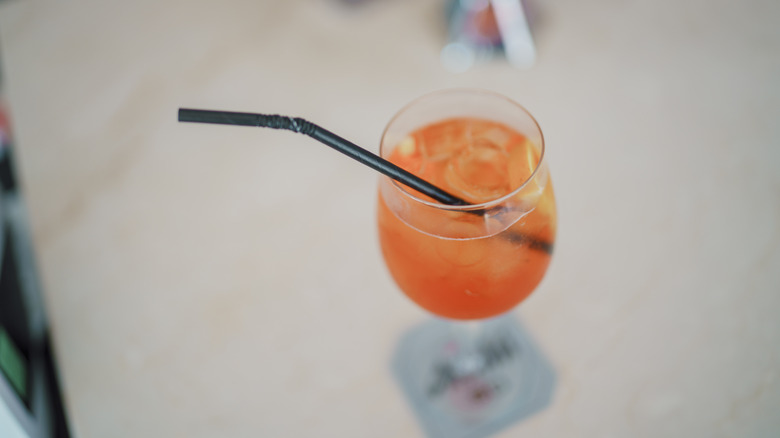 An overview shot of a prosecco-based cocktail that contains ice and a plastic straw