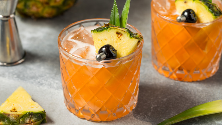 A rum cocktail in a tumbler with fresh fruit added to it and a measuring cup in the background