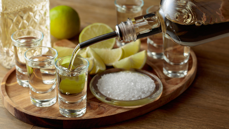 Shots of tequila poured onto a wooden tray that also contains salt and slices of lime