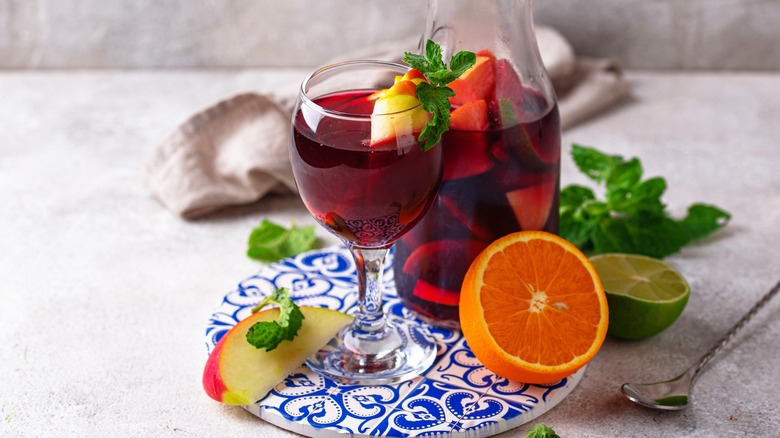 A glass of sangria surrounded by some of the ingredients that can be added to the drink