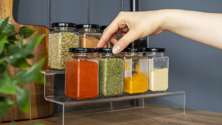 Hand picking up jar of dried herbs from spice rack