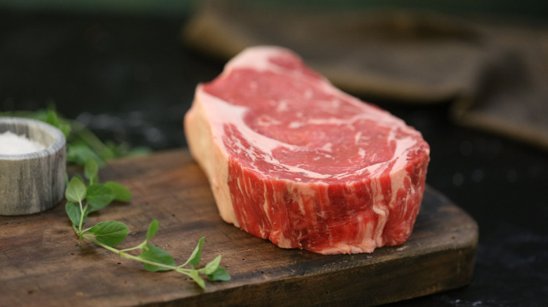 Thick ribeye with sprig of herb and salt on wooden board