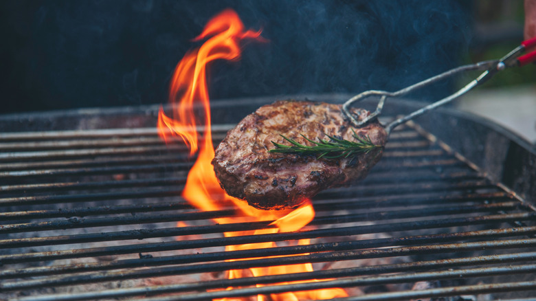Tongs moving steak on fiery grill