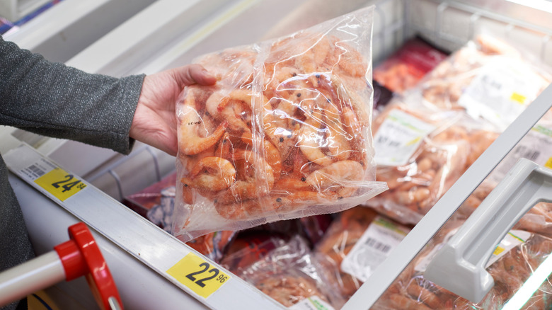 hand pulls frozen bag of shrimp out of store's freezer case