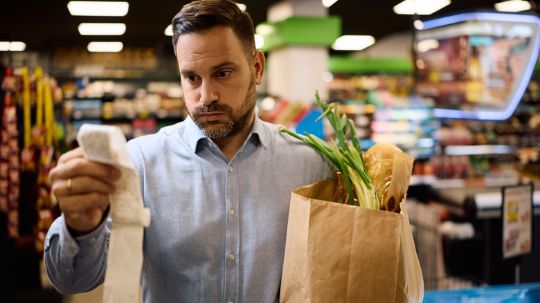 worried man looks at long grocery bill in store