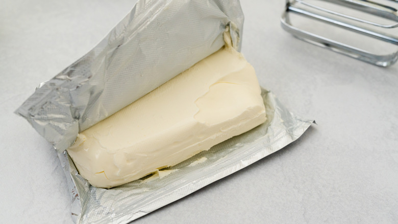 Opened block of cream cheese in foil wrapper next to metal beater