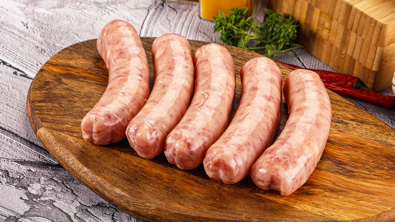 Five raw sausages lined up on wooden cutting board