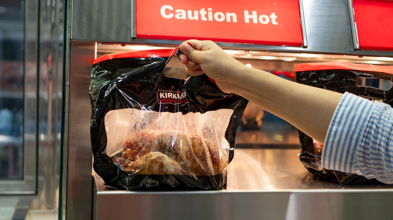 Hand taking Costco rotisserie chicken off of shelf