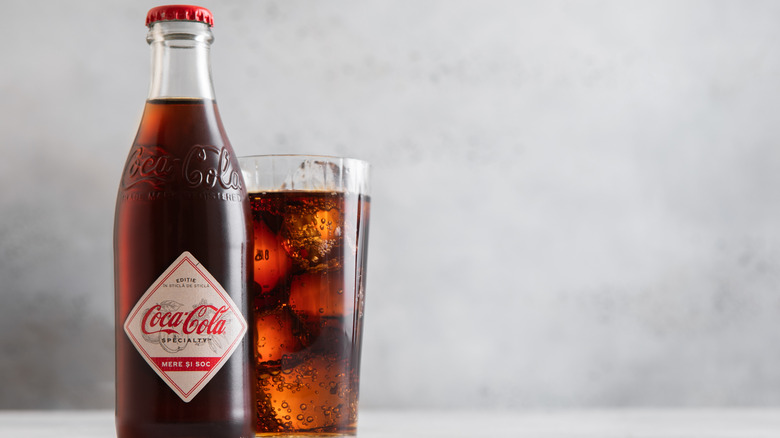 LONDON,UK - JULY 21,2025: Glass bottle of Vintage Retro Original taste Coca-Cola soft soda drink with glass of ice cubes on light table.