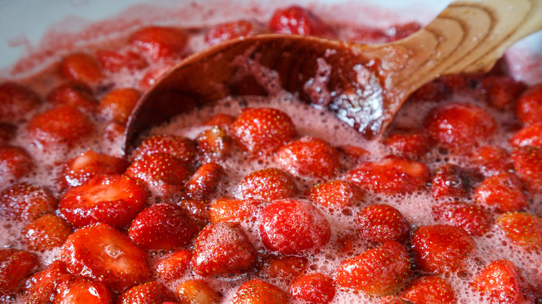 Making homemade strawberry jam. Boiling strawberry jam with a wooden spoon close-up. Red sweet syrup. Soft Focus, Close Up.