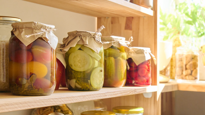 Storage of food in kitchen in pantry. Wooden cabinet with jars and containers, cereals, spices, paste, nuts, canned pickled fruits and vegetables, kitchen utensils. Eat at home, stock food concept.