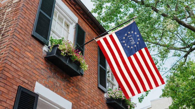 Close-up of Betsy Ross 1776 flag hanging from upper window of brick house.
