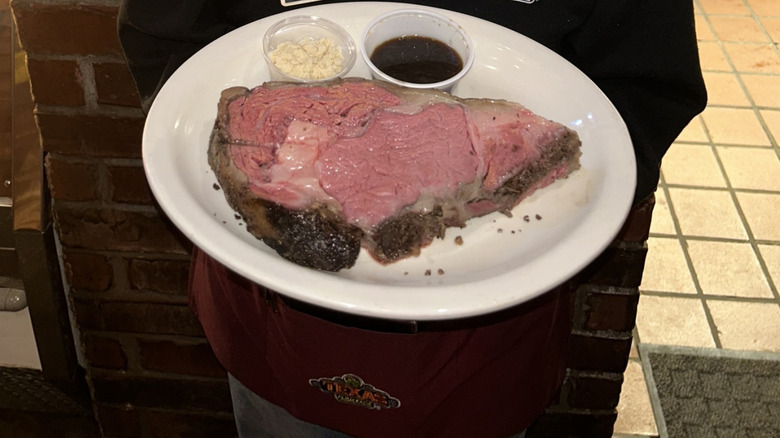 Person holding Texas Roadhouse prime rib on white plate