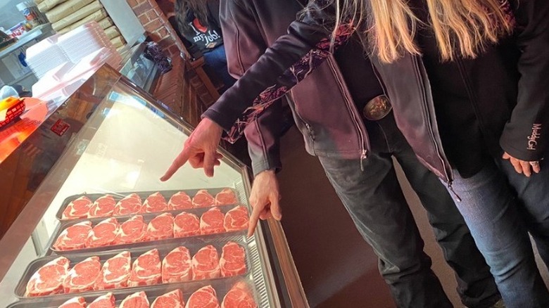 Hands of Texas Roadhouse patrons pointing at steak in display case