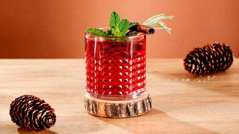 A red fall cocktail garnished with rosemary, mint, and a cinnamon stick
