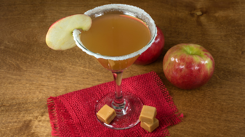 An apple slice on a martini with apples and caramel chunks next to it
