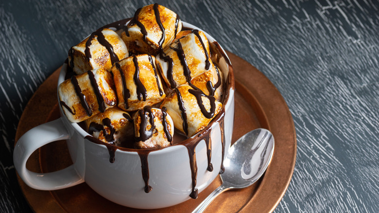 A hot drink in a mug, topped with toasted marshmallows and drizzled chocolate syrup