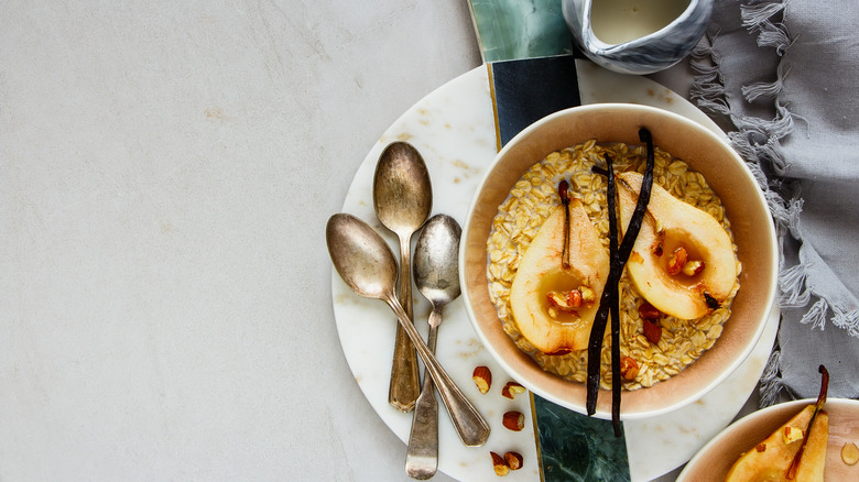 Bowl of oats topped with pear and vanilla beans, on plate with three spoons