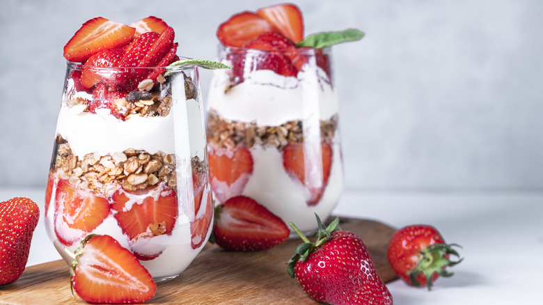 Two parfait glasses filled with yogurt, strawberries, and granola