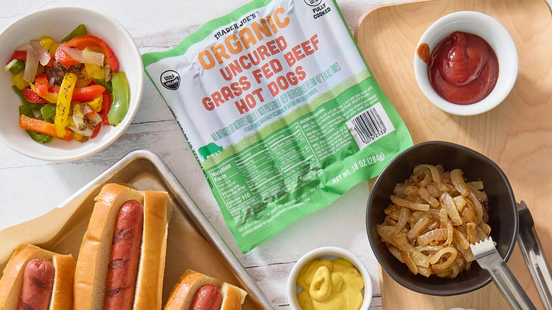 Package of Trader Joe's Organic Uncured Grass Fed Beef Hot Dogs beside hot dogs, toppings, and condiments