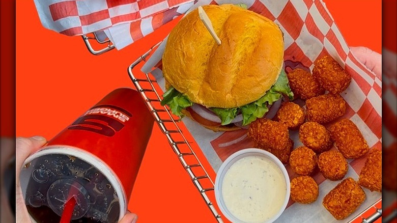 Smashburger burger with tater tots, dipping sauce, and soda.
