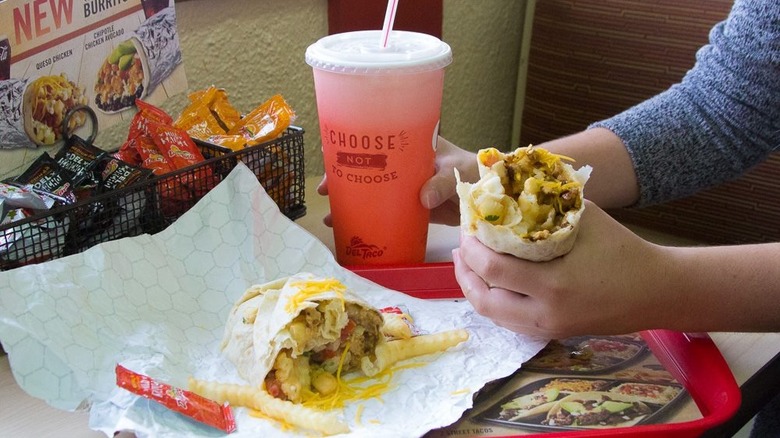 Hand holding breakfast burrito over tray at Del Taco