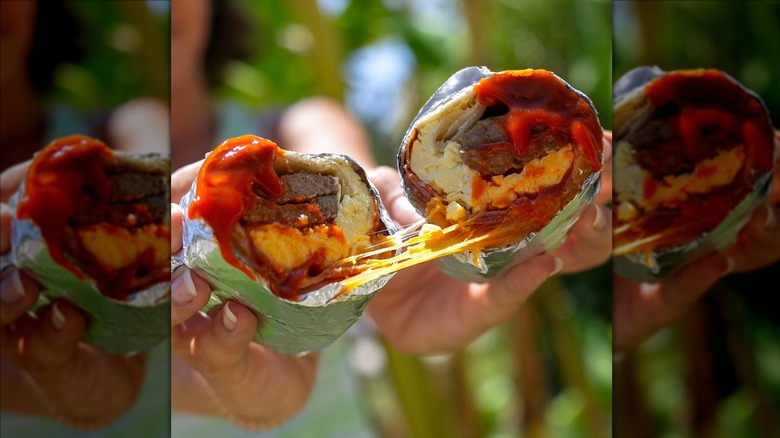 Hands pulling apart a Jack in the Box breakfast sandwich