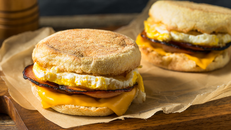 Two breakfast sandwiches on parchment paper on wooden cutting board