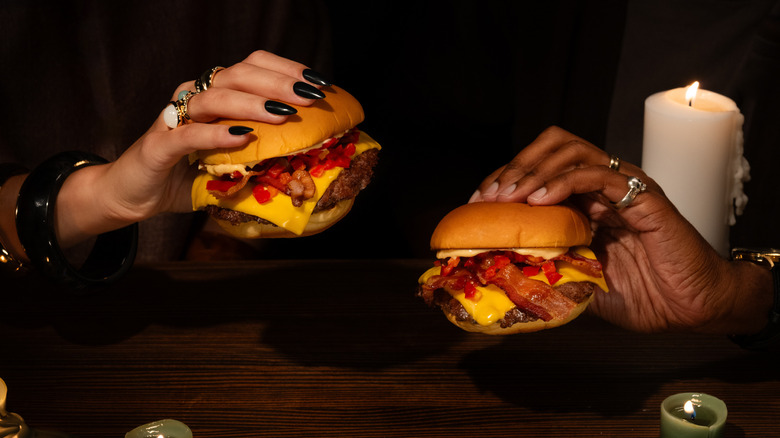 Two hands holding Shake Shack SmokeShack burgers.