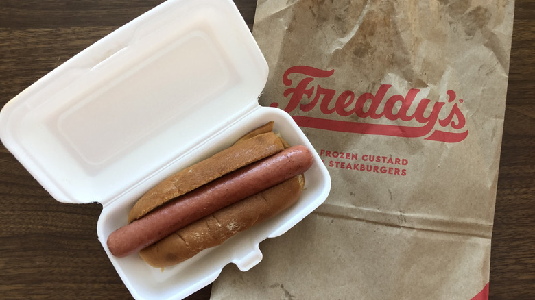 Freddy's Vienna all-beef plain hot dog in styrofoam box and to-go bag.