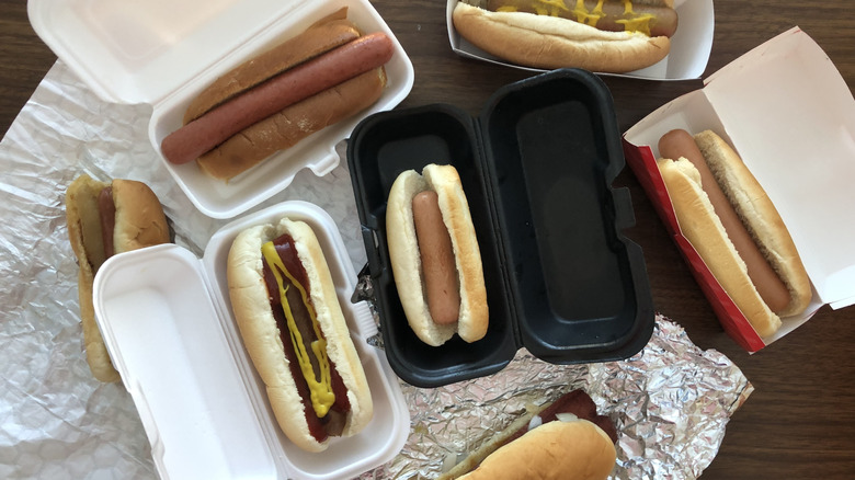 Seven different fast food restaurant hot dogs in their boxes and wrappers.