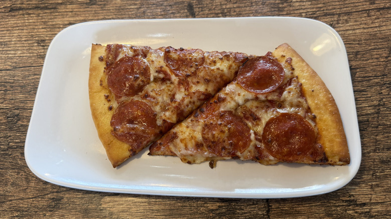 Two slides of Fazoli's pepperoni pizza served on a white rectangular plate placed on a wooden counter