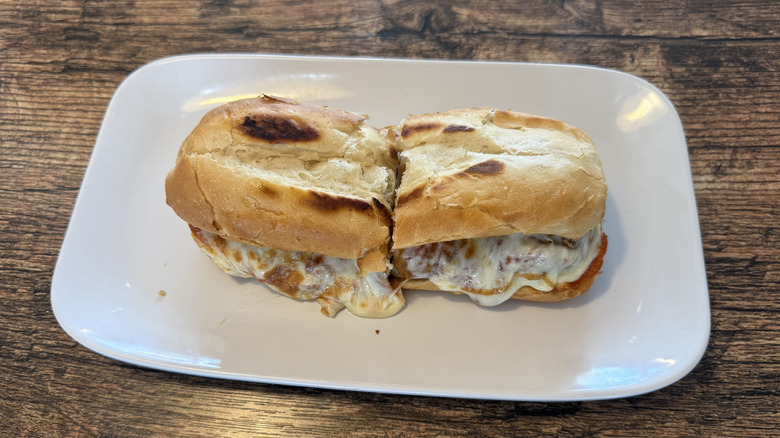 Fazoli's meatball sub sliced in half with the cheese oozing out that is served on a white rectangular serving dish that is placed on wood