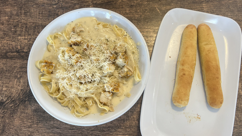 Fazoli's chicken fettuccine alfredo served in a white plate with two breadsticks served on the side on a separate rectangular plate