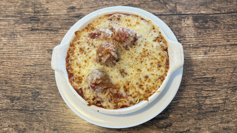 Top view of Fazoli's spaghetti and meatballs dish on wood table served in a white bowl with a cheesy layer on top