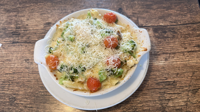 Fazoli's chicken broccoli penne on a wooden table served in a round dish with grated cheese on top and some cherry tomatoes
